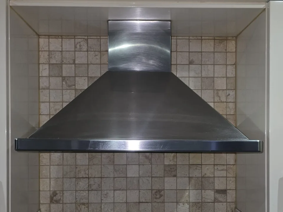 Stainless steel extractor hood between white kitchen cabinets